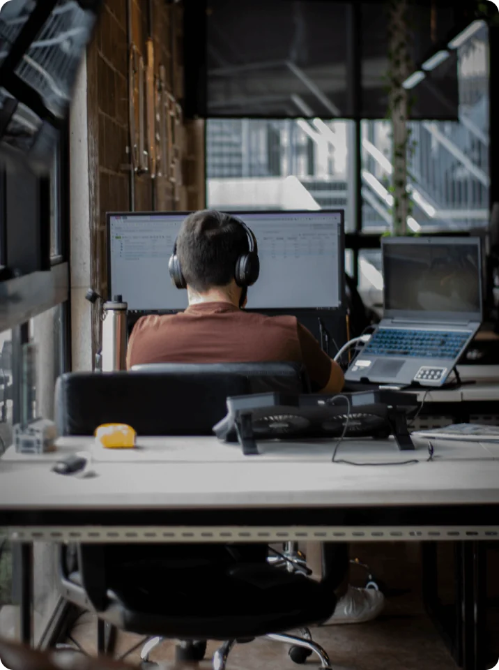 Cluster team member wearing headphones at a workstation with a monitor and laptop in the company office